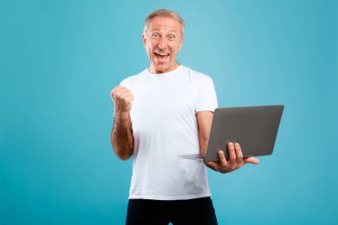 Neşeli, olgun bir adam heyecan ve neşe gösterirken elinde bir dizüstü bilgisayar tutuyor. Yumruğunu sıkarak zafer işareti yapıyor. Parlak mavi bir stüdyoda büyük haberi kutluyor..