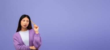 Mor kazaklı bir kadın elinde kalem tutarken düşünceli görünüyor. Sakin bir ifadeyle, katı mor bir arkaplan karşısında duruyor. Derin düşüncelere ya da fikir üretimine işaret ediyor..