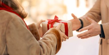 Bir insan, kırmızı bir yayla süslenmiş bir hediyeyi başka bir kişiye verir ve kış ayinlerinde bir sevinç anı yaratır. Yumuşak kar, şenlikli atmosfere ekleniyor..