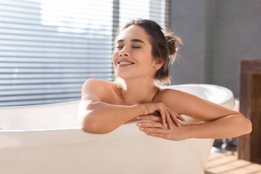 Genç bir kadın lüks bir banyoda sıcak bir banyodan zevk alıyor. Kapalı gözlerle küvette rahatça oturuyor. Rahatlatıcı atmosferin tadını çıkarıyor. Huzurlu ve yenilenmiş hissediyor..