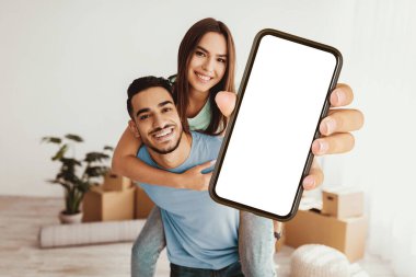 Genç bir çift, kadını sırtında taşıyan adamla kapalı alanda keyifli bir anı paylaşıyor. Adam elinde bir akıllı telefon tutarken kameraya gülümserler, eğlenceli anıları yakalamaya hazırdırlar..