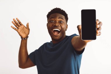 Geniş tebessümlü genç bir adam heyecanla akıllı telefonunu önünde kaldırıyor. Sıradan bir mavi gömlek giyiyor ve özel bir anı kutluyor gibi görünüyor..