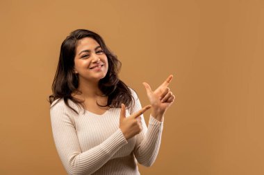 Harika bir tanıtım. Mutlu Arap kadın iki eliyle fotokopi alanını işaret ediyor, genç ortadoğulu bayan kahverengi arka planda sizin ilanınız ya da mesajınız için boş alan gösteriyor.