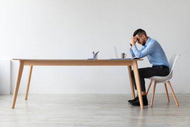 Genç bir Arap adam rahatsız bir şekilde masasında oturuyor. Parlak ve modern bir ofiste bilgisayar üzerinde çalışırken stresli görünüyor. Sahne, odaklanmak için verdiği mücadeleyi yakalar..