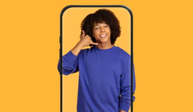 Kıvırcık saçlı, gülümseyen ve akıllı telefon çerçevesi içinde dururken telefonla konuşan biri. Parlak sarı arka plan sahneye canlılık katıyor..