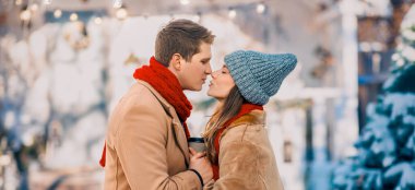 İki insan birbirine yakın durur, kar ve tatil süslemeleriyle dolu bir kış sahnesinde romantik bir öpücük paylaşırlar..