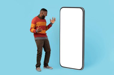 Great Deal. Excited Happy Black Male Looking At Big Blank Smartphone With Amazement, Cheerful Young African American Man Enjoying Online Offer, Standing On Blue Studio Background, Mockup