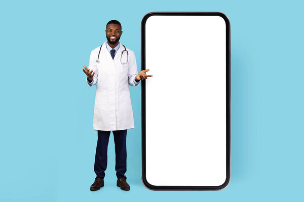 Telemedicine Concept. Black Doctor Standing Near Big Blank Smartphone With White Screen, African American Male Therapist Advertising Medical App, Posing Isolated On Blue Background, Mockup, Collage