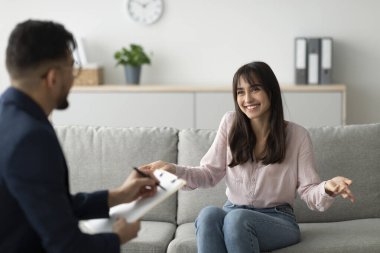 Özel bir terapi seansında, orta doğulu bir kadın gelişimini bir koltukta rahat bir şekilde otururken psikoloğuyla coşkuyla paylaşıyor. Konuşurken gülümsüyor.