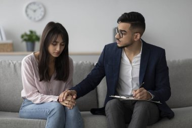 Profesyonel bir psikoterapist, depresyondaki bir Arap kadın hastasını klinik ortamında rahatlatır. Eğitimli danışman seans boyunca meşgul ve özenli, duygusal destek sağlıyor..