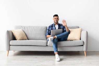 Mutlu bir Arap adam evdeki bir kanepede oturur ve arkadaşları ya da ailesi ile görüntülü bir görüşme yapar. Dizüstü bilgisayara el sallıyor, bir neşe ve bağlantı hissi veriyor..