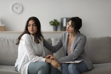 Ruh sağlığı kliniğinde, şefkatli bir psikolog üzgün bir Arap kadını nazikçe rahatlatır..