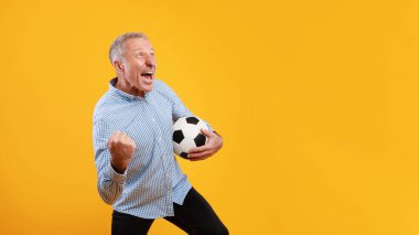 Olgun bir adam sarı bir zemine karşı duruyor, elinde futbol topu ve tezahürat yapıyor. Eğlenceyi ve heyecanı ifade eder, futbol maçını izlemenin heyecanını gösterir..
