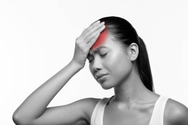 Hasta genç kadın, koronavirüsün sebep olduğu ateşi azaltmak için alnına dokunuyor. Bu yakın plan beyaz bir arkaplan karşısında rahatsızlığını vurguluyor, hastalığının ifadesine odaklanıyor..