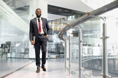 Ofis binasının önünden geçen, elinde dizüstü bilgisayarla yürüyen, fotokopi alanına bakıp gülümseyen, meslektaşlarıyla konferansa giden, panorama, tam boy...