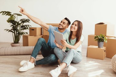 Mutlu bir çift yeni evlerinin zemininde otururlar ve etrafları kutularla çevrilidir. Bir tablete bakıyorlar, adam heyecanlı bir şekilde bir şeyi işaret ediyor, birlikte neşeli bir anı paylaşıyor..