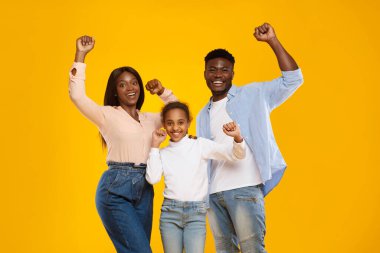 Üç çocuklu heyecanlı zenci aile kutlama için yumruklarını sallıyor. Parlak sarı-turuncu bir stüdyodalar, bu zafer anında mutluluğu ve birliği temsil ediyorlar..