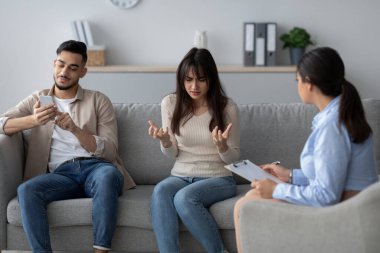 Terapi seansında, sinirli bir kadın kocasının akıllı telefon bağımlılığından duyduğu hayal kırıklığını dile getirir..