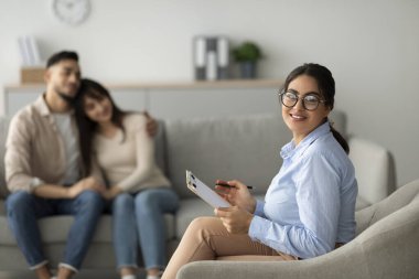 Bir evlilik danışmanı, ofisinde Orta Doğulu bir çiftle yaptığı etkili bir seanstan sonra gülümsüyor. Çift rahat ve bağlı görünüyor, terapilerinin olumlu sonucunu gösteriyor..