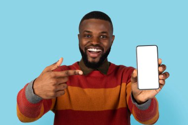 Online Offer. Excited Black Man Pointing At Big Blank Smartphone In His Hand, Cheerful African American Guy Demonstrating Phone With White Screen At Camera, Recommending New App, Collage, Mockup
