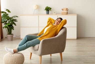 Mutlu bir ortadoğu kadını evinde rahat bir koltukta dinlenirken görülüyor. Elleri başının arkasında rahatça oturur, kameraya gülümser ve huzurlu bir hafta sonunun tadını çıkarır..