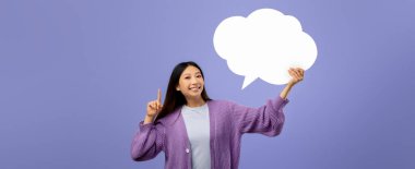 Genç bir kadın elinde kocaman boş bir konuşma balonu tutarken gülümsüyor. O rahat mor bir kazak giyiyor ve uzun siyah saçları var..