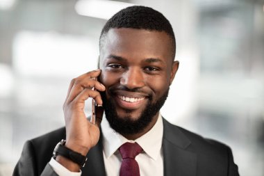 Ofiste çalışırken, kameraya bakıp gülümserken, iş ortağıyla akıllı telefondan konuşan şık takım elbiseli, yakışıklı, genç iş adamının yakın çekimi.