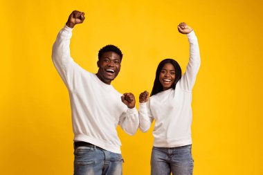 İki genç yetişkin bir arada durarak mutluluk ve heyecanı ifade ediyor. Sıradan beyaz eşofman üstü ve kot pantolon giyerler. Havalı yumruklar ve parlak gülücüklerle coşku gösterirler..