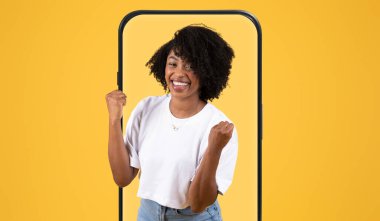 Neşeli genç bir kadın, neşeli bir poz vererek, kutlama için yumruklarını kaldırırken geniş bir gülümseme içinde duruyor. Canlı sarı arkaplan sahneye enerji katıyor..