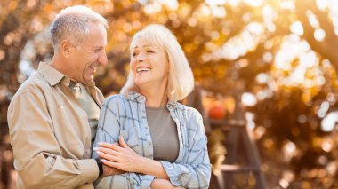 İki yetişkin, renkli sonbahar yapraklarıyla dolu bir parkta mutlu bir anı paylaşıyor. Birbirlerine sıcak bir şekilde gülümserler, doğaları gereği güzel güneş ışıl ışıl parlar..