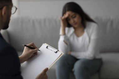 Bir tıp bürosunda, orta doğulu bir kadın bir psikologla görüşürken sıkıntı belirtileri gösterir. Psikiyatrist, oturum sırasında destek sağlayarak bir panoya notlar alır..