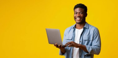 Genç bir adam dizüstü bilgisayarıyla güvenle ayakta duruyor ve sevinçlerini ifade ediyor. Parlak sarı arka plan, teknolojiye ve bağlantıya olan hevesini göstererek sahneye enerji katıyor..