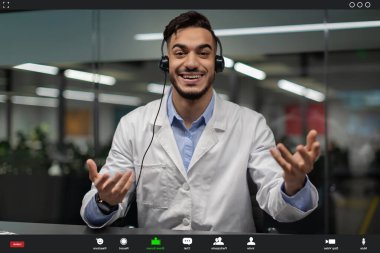 Laboratuvar önlüğü giyen genç bir ortadoğulu bilim adamı bir video görüşmesi sırasında iş arkadaşlarıyla mutlu bir şekilde konuşuyor..