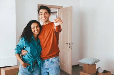 Mutlu çift, yeni evlerinin anahtarlarını tutarak aydınlık bir odada birlikte duruyorlar. Taşınan kutularla çevrili olarak hayatlarında yeni bir sayfa açma heyecanı ve tebessümü paylaşıyorlar..