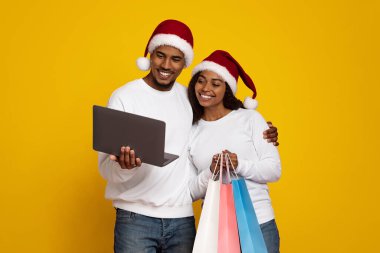 Mutlu bir çift, parlak sarı bir arkaplan önünde dizüstü bilgisayar ekranına bakarak yan yana durur..