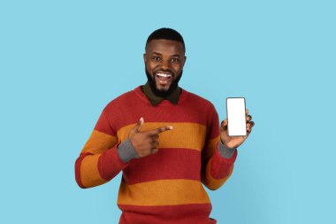 Mobil Teklif. Yakışıklı siyah erkek elinde boş beyaz ekranla telefonu işaret ediyor, gülümseyen Afrikalı Amerikalı bir adam yeni bir uygulama ilanı veriyor, mavi arka planda tek başına duruyor,