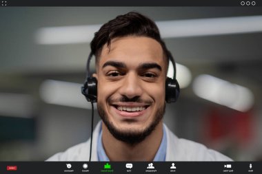 Görüntülü bir aramada gülümseyen genç bir ortadoğu doktorunun yakın çekimi. Kulaklık takıyor ve hastayla iletişim kuruyor. Modern sağlık hizmetleri iletişimini gösteriyor..