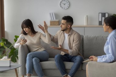 Kızgın bir çift ilişki sorunlarını bir terapistle tartışıyor. Kadın telefonuna odaklanmış gibi görünürken, erkek anlamlı bir şekilde el kol hareketi yapar..