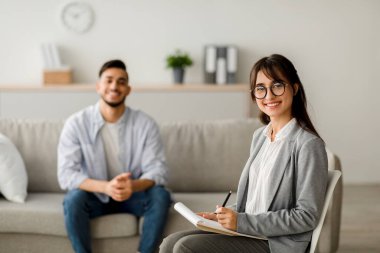 Kendine güvenen bir Arap kadın psikolog not alırken kameraya gülümsüyor. Orta Doğulu genç bir adam rahat bir şekilde oturur ve başarılı terapi seanslarından sonra gülümser..