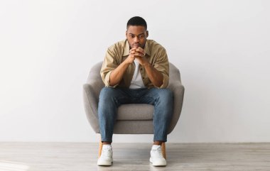 Gri Duvar Arkaplanı 'nın üzerinde oturan düşünceli Afrikalı Amerikalı adam. Düşünceli Milenyum Adamı 'nın Sorunları Yansıtan Uzun Boylu Çekimi, Ön Görünüm