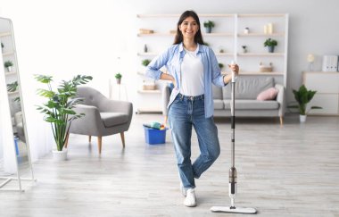 Temizlik işi konsepti. Günlük kıyafetlerle gülümseyen genç bir kadın ahşap kaplamaları yıkıyor modern paspas kullanıyor, ev ödevi temizliyor mutlu bir kadın poz veriyor ve kameraya bakıyor.