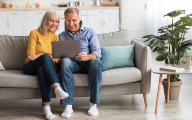 Neşeli Son Sınıf Eşleri İnternette Laptop İzliyor ya da Evdeki Kanepede Oturan İnterneti İzliyor. Yaşlılar ve Gadget 'lar, Modern Emeklilik Yaşam Tarzı Konsepti