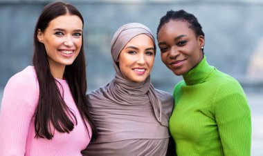 Üç tane çok ırklı genç kadının portresi. Afro-Amerikan, Müslüman ve Kafkasyalı kadınlar dışarıda birbirlerine sarılmışlar kameraya bakıp gülümsüyorlar. Birlik ve Çeşitlilik