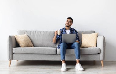 Rahatla konsept. Mutlu bir adam evdeki rahat koltukta oturup kahve içerek rüya görüyor. Keyifli rahat bir adam kanepede dinleniyor, hafta sonunun keyfini çıkarıyor, tüm vücut uzunluğuyla.