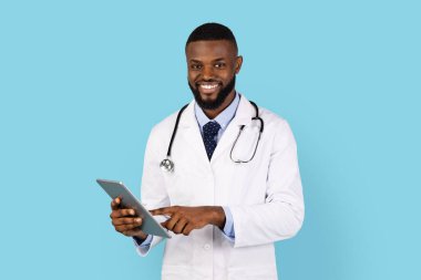 Modern Tıp Bölümü. Mavi stüdyoda dijital tabletle poz veren gülümseyen siyah doktor, modern Gadget kullanan ve kameraya gülümseyen Afrikalı Amerikalı doktor,