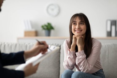 Müteşekkir bir Arap bayan müvekkil modern bir ofiste rahat bir şekilde oturuyor, gülümsüyor ve psikoloğuyla görüşüyor. Aldığı destekleyici terapi için minnettarlığını ifade ediyor..