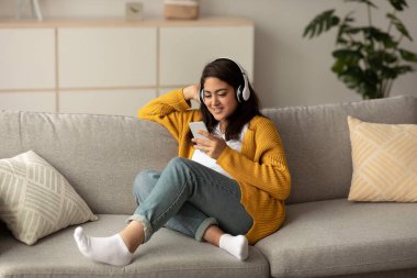 Pozitif Arap bayan koltukta rahatça oturur, kablosuz kulaklık takar ve akıllı telefonuyla müzik dinler. Uygulamayla meşgul ve mutlu görünüyor, boş zamanlarının tadını çıkarıyor..