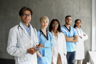 En yeni modern klinik ya da hastanenin çok ırklı profesyonel ekibi iş kıyafetlerindeki erkek ve kadınların kamera karşısında gülümseyerek takım oluşturma ya da tıp konferansına katılmaları,