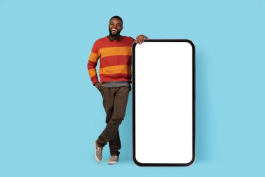 Mobil Model. Big Blank Smartphone 'a yaslanan mutlu siyah erkek, Afrikalı Amerikalı bir adamın boş beyaz ekranlı, yaratıcı kolajlı, sahte resimli büyük bir telefonun tam uzunluğunda fotoğrafı.