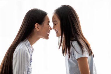 Burunlarına dokunan genç bir kadınla kızı arasında sevgi dolu bir etkileşim gerçekleşir. Her ikisi de gülümsüyor, güçlü bağlarını ve mutluluklarını beyaz bir arka plana karşı sergiliyorlar..